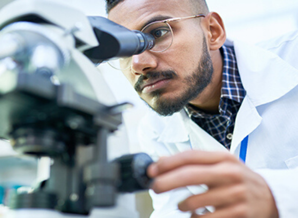 Man In A White Coat Looking Through A Microscope