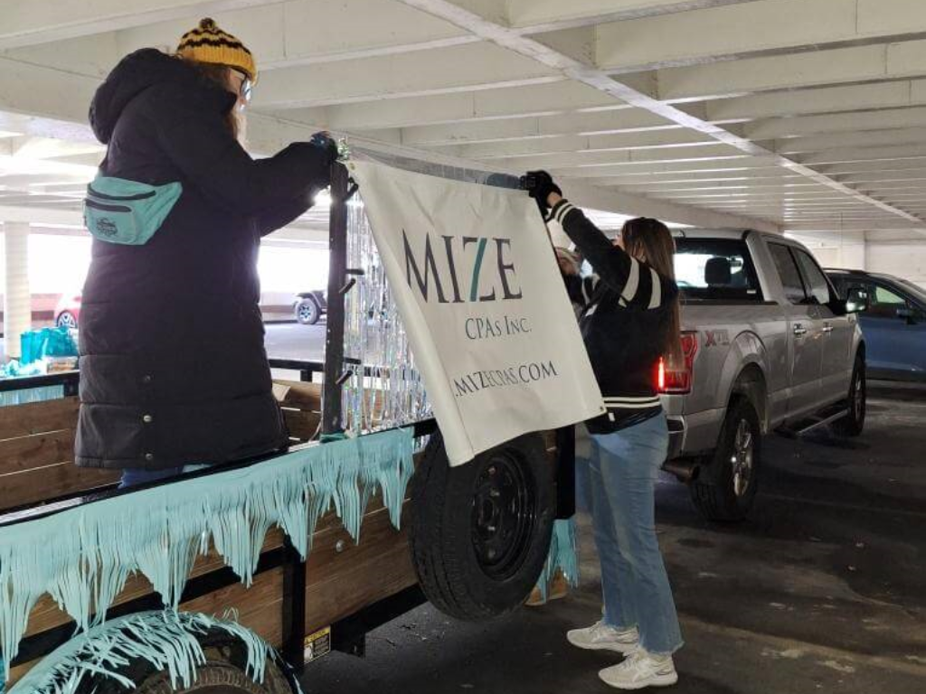 Two People Putting Mize CPAs Banner On A Tailer For A Float