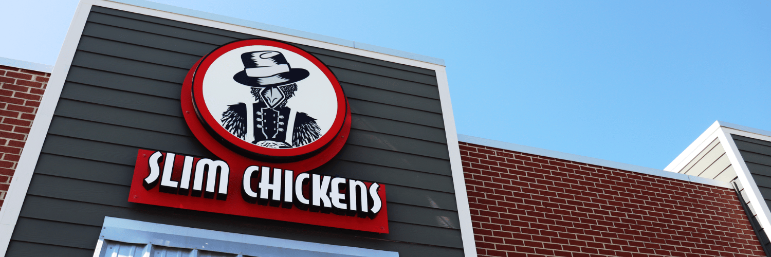 Photo of Slim Chickens restaurant focused on the Slim Chickens logo with metal awning and red brick building