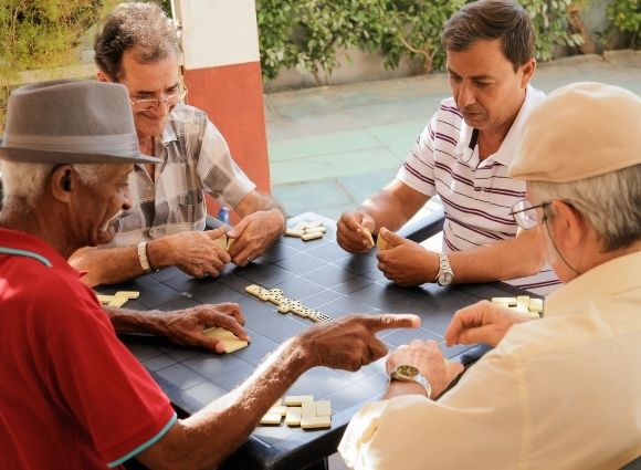 Four Older Men Playing Dominoes At A Atable Outside