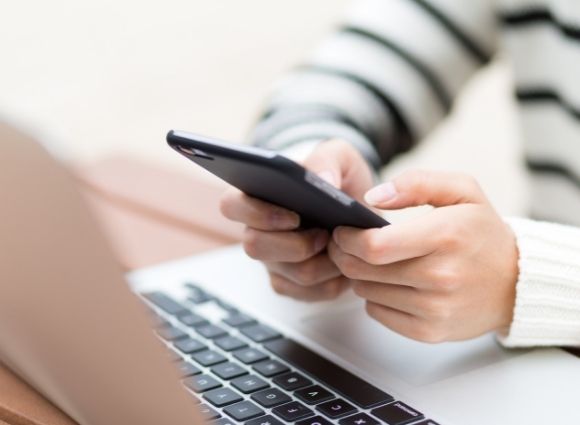 Young Person Holding Cell Phone And Texting In Front Of A Laptop