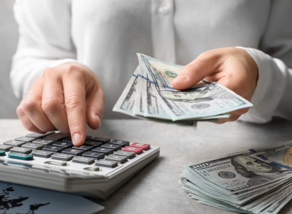 Photo Of A Person Holding Cash And Entering Numbers Into A Calculator