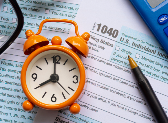 Orange Clock Laying On A Form 1040 And Other Tax Documents