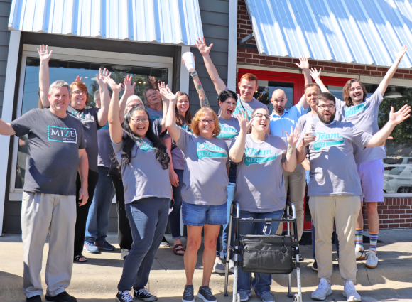 Team Mize Celebrating With Their Hands In The Air In Front Of A Slim Chickens Restaurant