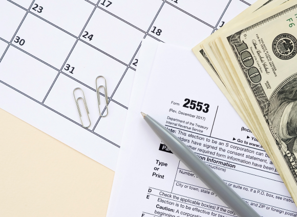 An Image Of Form 2553 With A Pen, A Calendar, And $100 Bills.